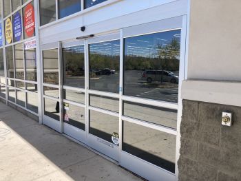 Empty storefront entrance with glass doors and windows along a sidewalk in a strip mall